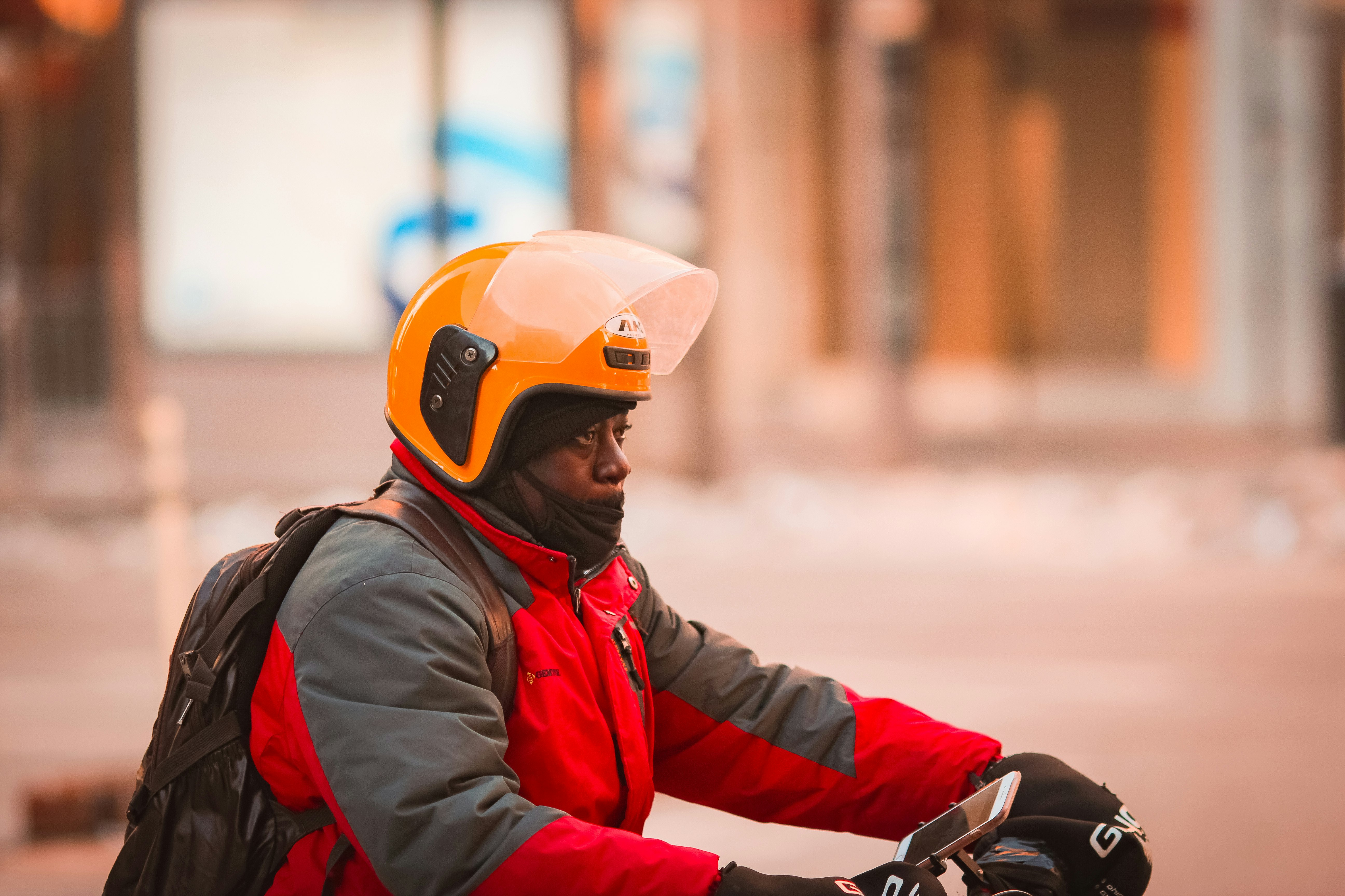 man in red and black jacket wearing orange helmet riding on motorcycle during daytime